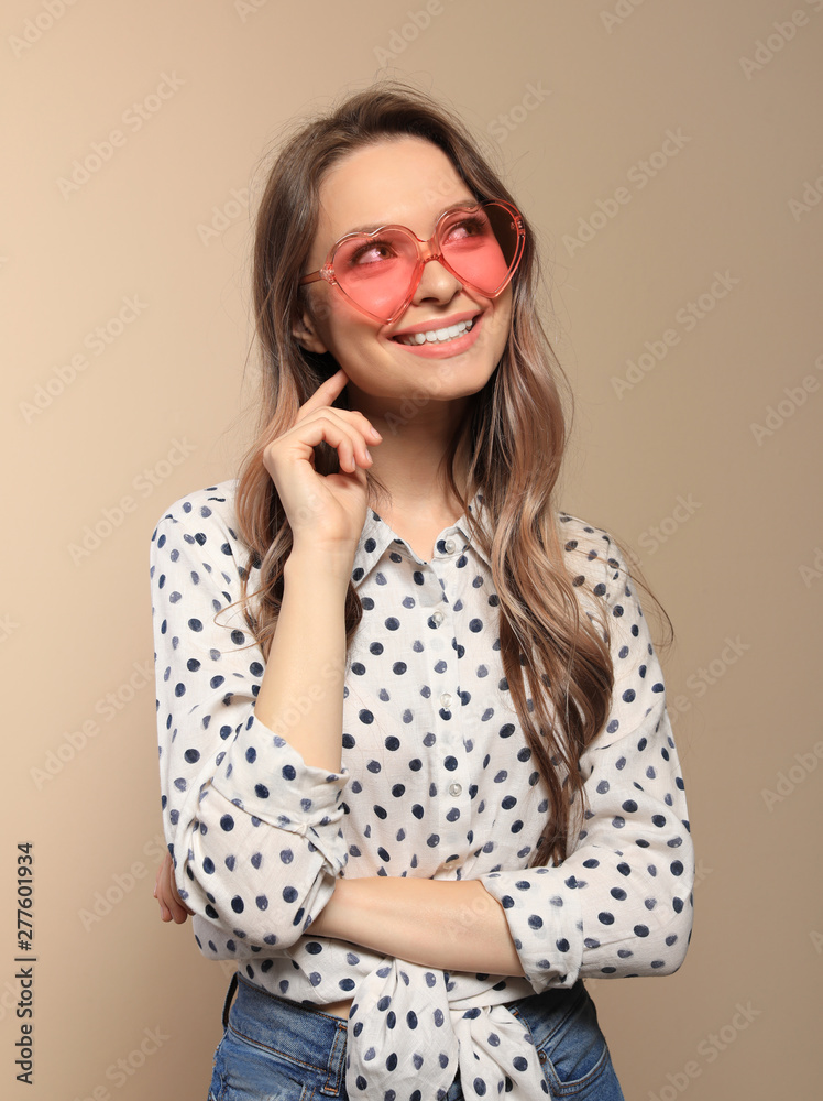 Portrait of beautiful young woman with heart shaped sunglasses on color background