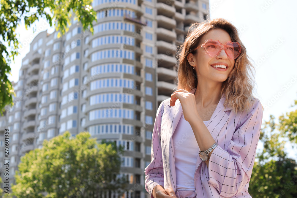 Portrait of happy young woman with heart shaped glasses in city on sunny day. Space for text