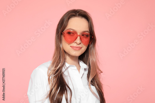 Portrait of beautiful young woman with heart shaped sunglasses on color background © New Africa
