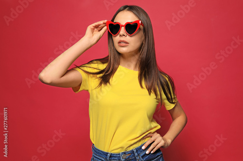 Portrait of beautiful young woman with heart shaped sunglasses on color background