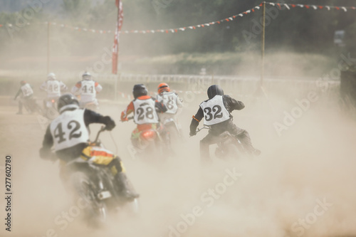 Racing motorcycles making a lot of dust when accelerating after the turn on the dirt racing track.