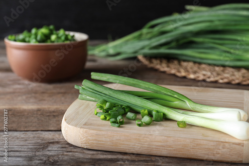 Wooden board with fresh green onions on table