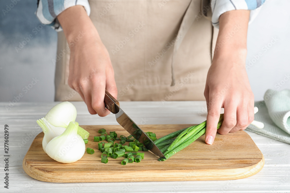 Woman cutting fresh green onion on wooden board at table, closeup Woman cutting fresh green onion on wooden board at table, closeup