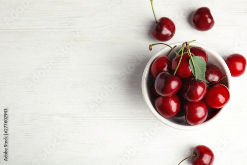 Bowl with sweet cherries on white wooden table, top view. Space for text photo