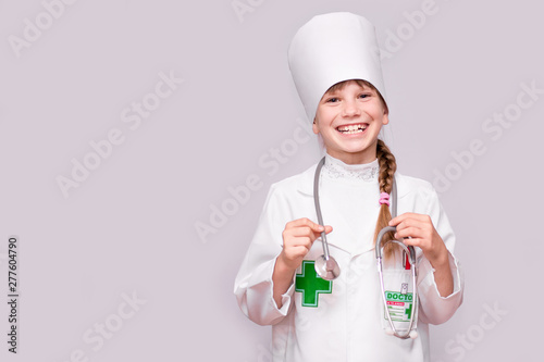 Smiling little girl in medical uniform holding stethoscope and looking at camera isolated on white
