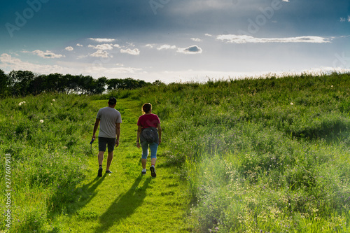 Couple hiking on trail with small dog at sunset in a grassland prairie with trailing shadows