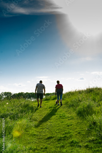 Couple hiking on trail with small dog at sunset in a grassland prairie with trailing shadows