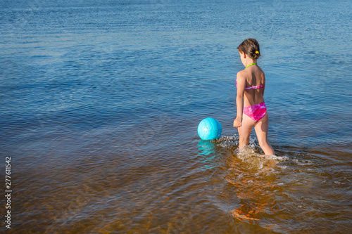 A little girl with blue ball playing in the water. A healthy way of life.