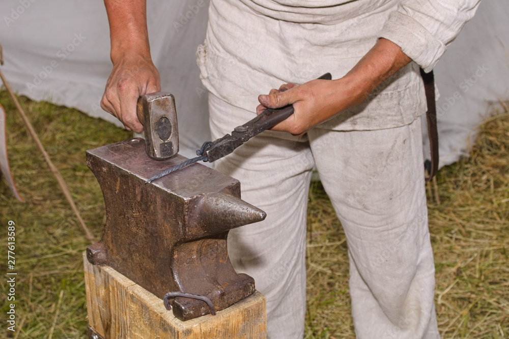 Blacksmith working with a hammer on the anvil in the open air. Forging metal products. Blacksmith working with a hammer on the anvil in the open air. Forging metal products.
