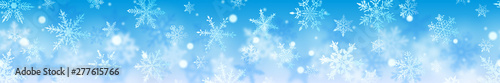 Christmas banner of complex blurred and clear snowflakes in white colors on light blue background. With horizontal repetition