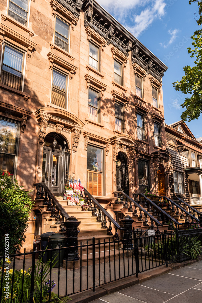 Scenic view of a classic Brooklyn brownstone block with a long facade and ornate stoop balustrades on a summer day in Brooklyn