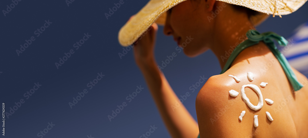 Woman tanning at the beach with sunscreen cream - obrazy, fototapety, plakaty 