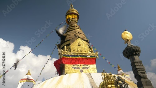SLOW MOTION: Pigeons fly away from the famous Monkey Temple in Nepal on a windy autumn day. Scenic view of a large buddhist stupa in Kathmandu with colorful prayer flags fluttering in the breeze.