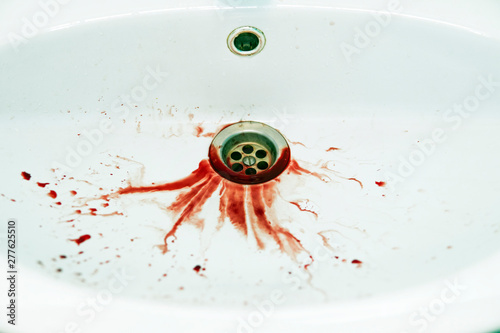 Red floods of blood dripple to the white washbasin drain. Bathroom sink is soiled with blood stains. Unhealthy state. Bleeding human has spitted into washbowl. Fatal outcome. Painful illness photo