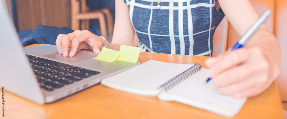 Woman hand working at a computer and writing on a notepad with a pen in the office.Web banner.