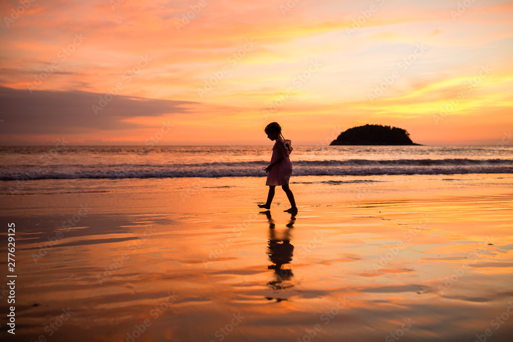 Cute little girl walking on the beach. Sunset time. Kid having fun in holiday vacation with back sun light - Youth, lifestyle, travel and happiness concept