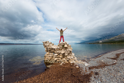 The girl stands on a pile of stones and looks at the sea.