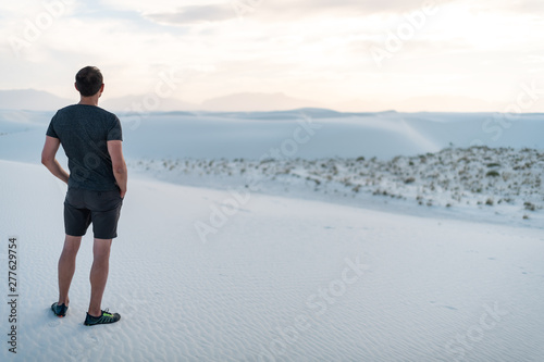 Man back standing on sand in white sands dunes national monument in New Mexico looking at sunset over horizon and Organ Mountains