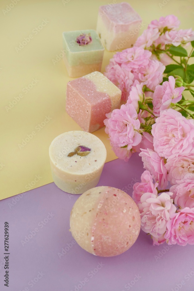 bath bombs set with rose extract and pink roses on a  yellow lilac mix background.Organic cosmetics for body