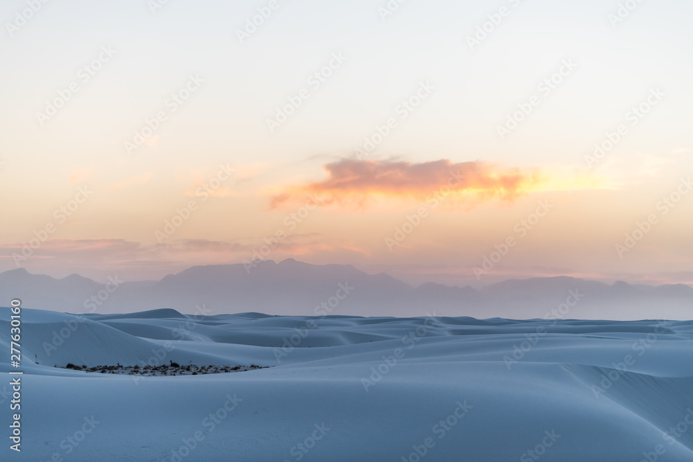 White sands dunes national park in New Mexico with horizon at sunset with silhouette of Organ Mountains and clouds