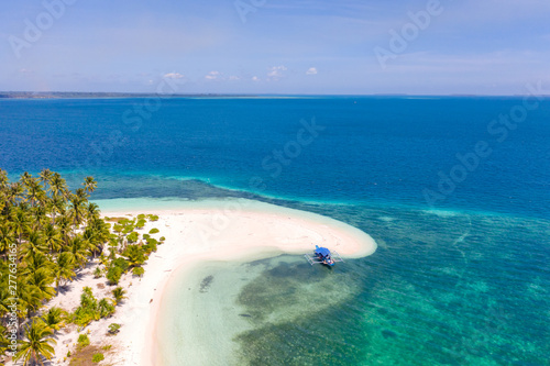Tropical island of white sand with coconut trees. Boat with tourists on a beautiful beach, aerial view. Seascape, nature of the Philippine Islands.