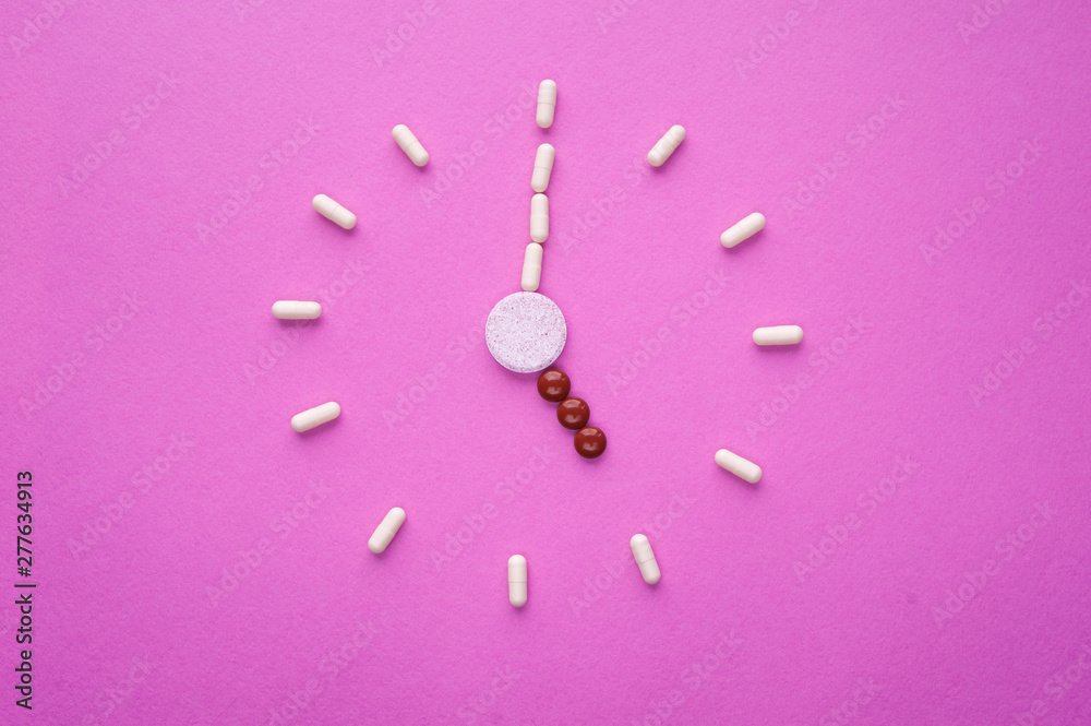 Clock created from white pills and brown tablets on pink background. Right time for using medicines. Brown and white capsules is five o'clock. Concept: medicine, drugs, healthcare, painkillers, time. Clock created from white pills and brown tablets on pink background. Right time for using medicines. Brown and white capsules is five o'clock. Concept: medicine, drugs, healthcare, painkillers, time.