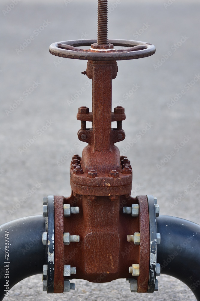 Huge rusty industrial wheel valve bolted to large bore pipes. Huge rusty industrial wheel valve bolted to large bore pipes.