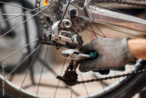 Cropped shot of repairman working in bicycle repair shop, mechanic repairing bike using special tool, wearing protective workwear and gloves