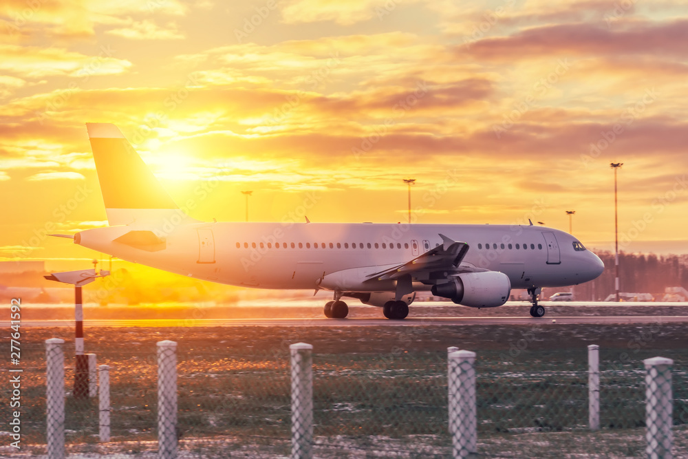 Passenger aircraft accelerates at the airport in the evening against the bright sun at sunset.
