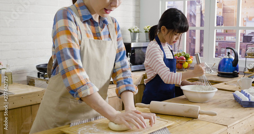 asian mom and daughter bake in kitchen for easter holidays. young elegant japanese wife unrecognized face hands kneading dough for bread on mothers day. cute little girl whisking egg in bowl.