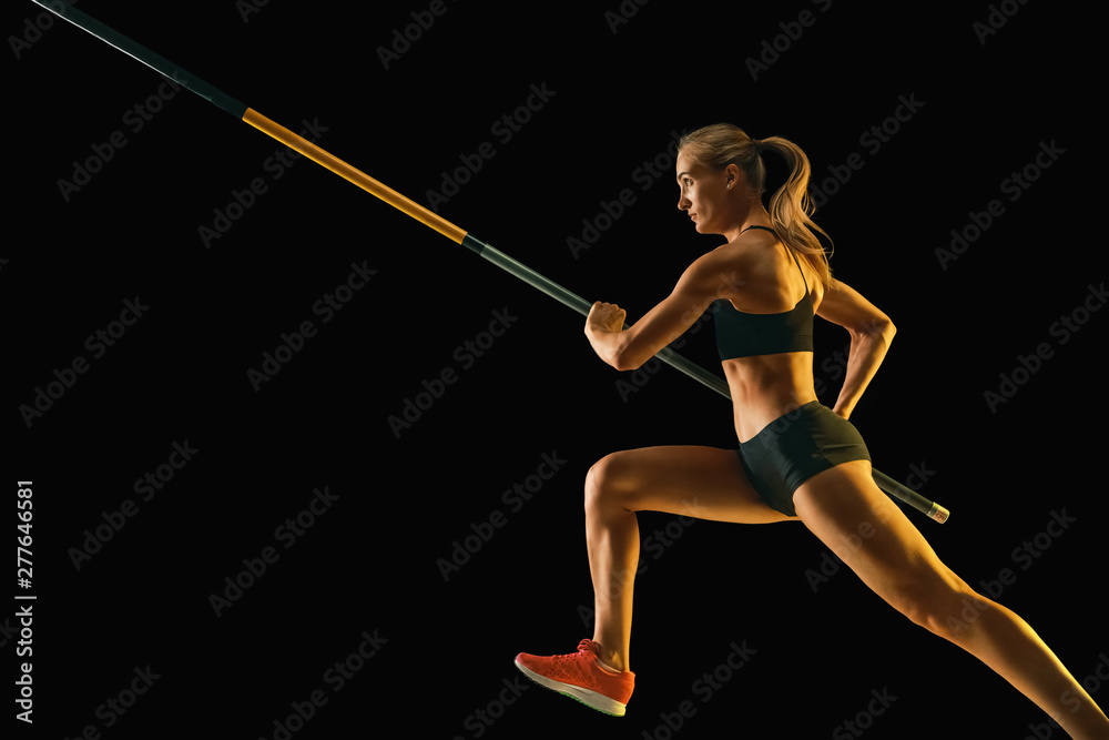Power and beauty. Professional female pole vaulter training on black studio background in neon light. Fit female model practicing. Concept of sport, healthy lifestyle, action, movement, motion. Power and beauty. Professional female pole vaulter training on black studio background in neon light. Fit female model practicing. Concept of sport, healthy lifestyle, action, movement, motion.