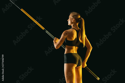 Power and beauty. Professional female pole vaulter training on black studio background in neon light. Fit female model practicing. Concept of sport, healthy lifestyle, action, movement, motion.