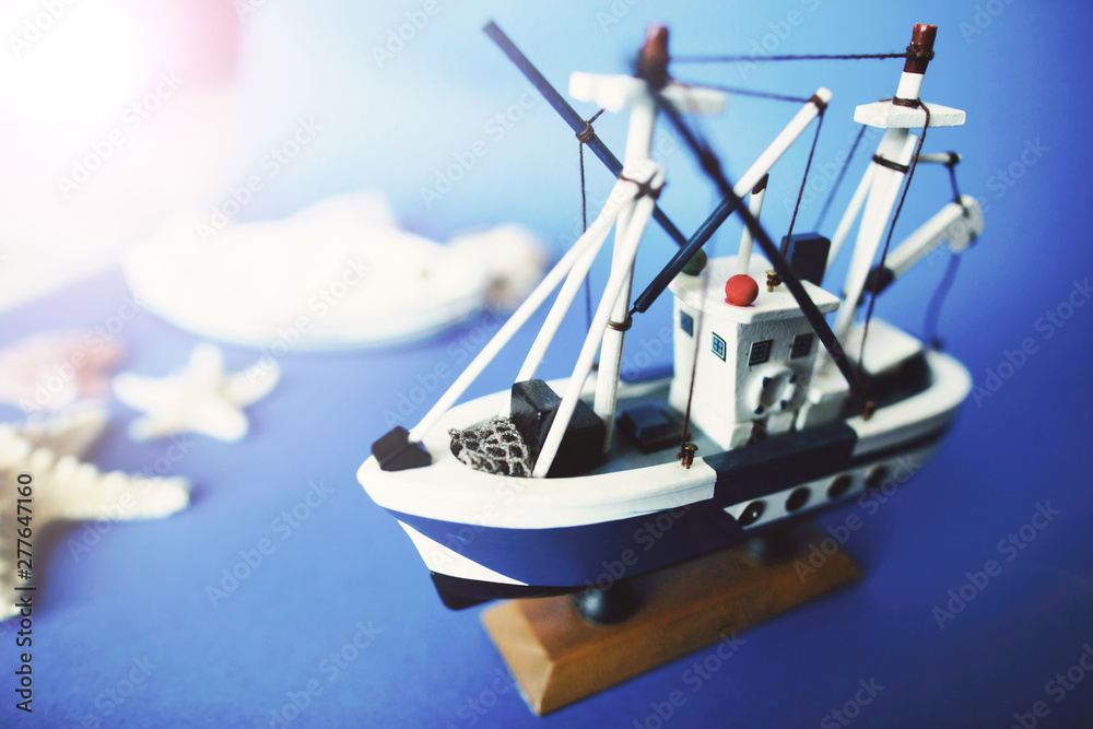 Little toy ship on a wooden stand with shells on a blue background. Copy space