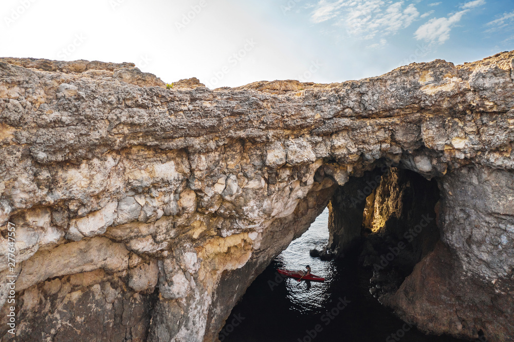 Big natural hole in the rock. Coral Lagoon in Mellieha. Kayak man. Malta island