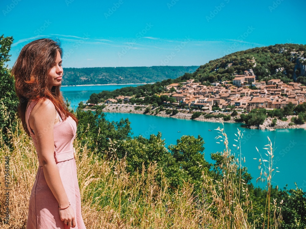 A girl with long hair in a pink dress stands on the background of the turquoise river durance in the South of France in Provence