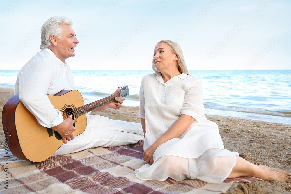 Mature man playing guitar for his wife at sea resort Mature man playing guitar for his wife at sea resort