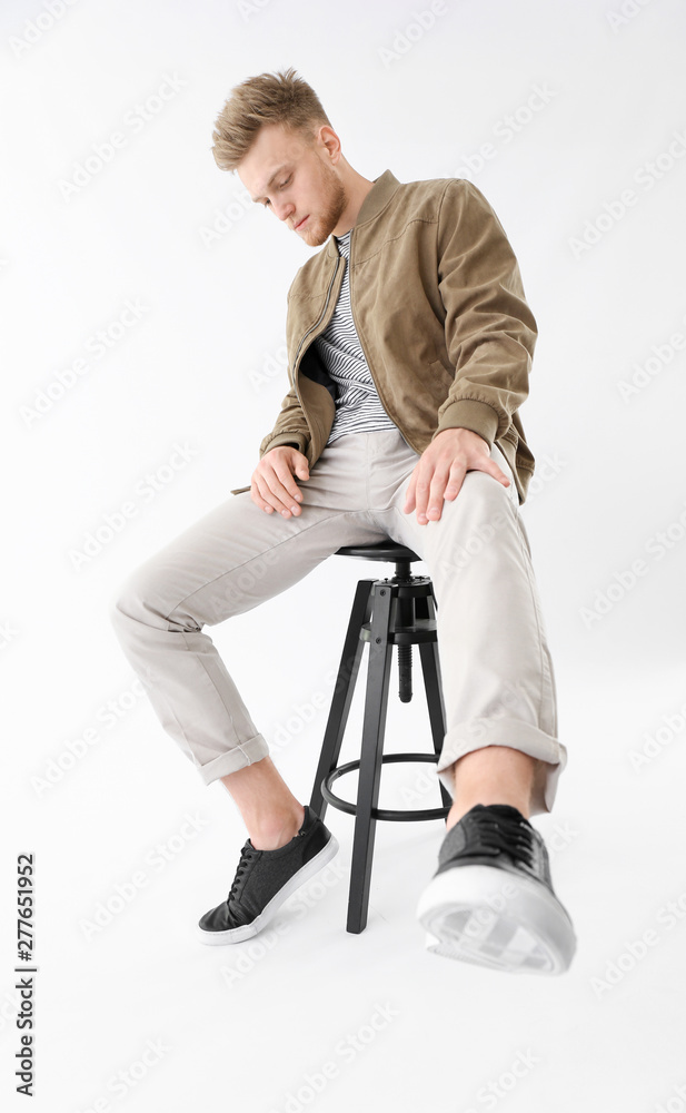 Stylish young man sitting on stool against white background