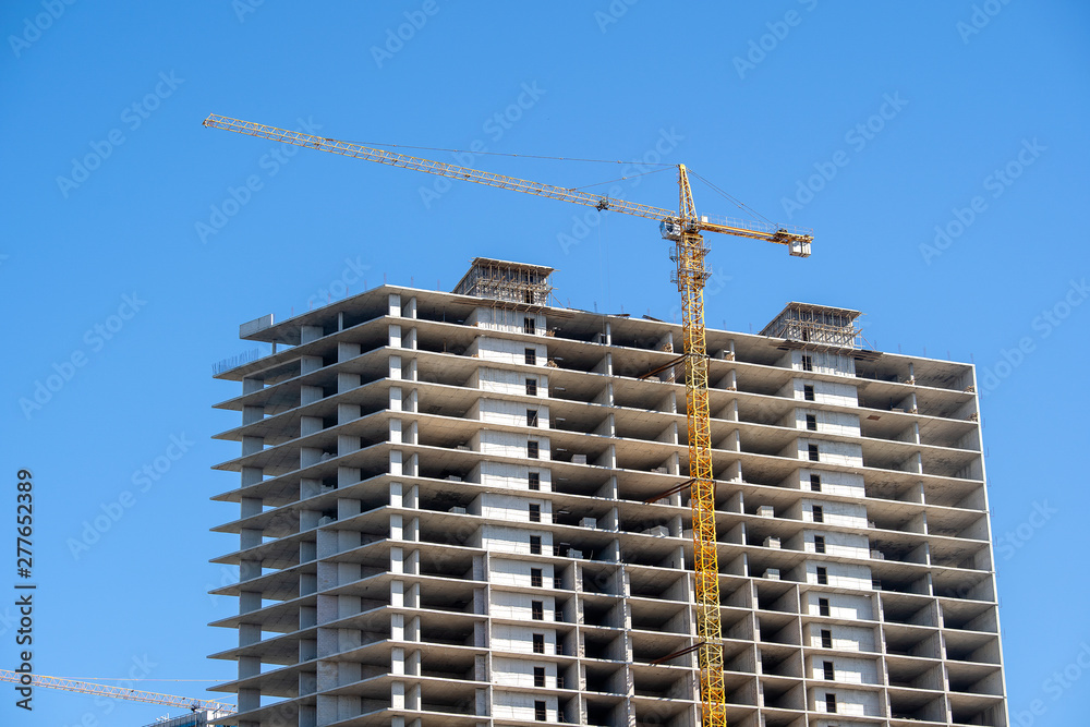 Fototapeta premium Construction of a high-rise building with a crane. The construction crane and the building against the blue sky.