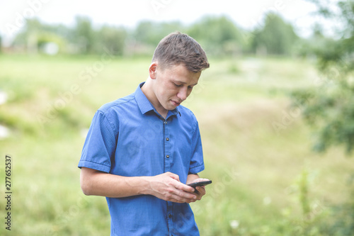 the guy in the blue shirt with the phone outdoors on a summer day