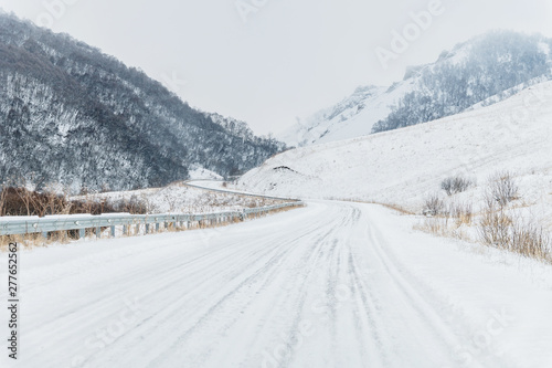 Empty mountain asphalt road in winter covered with snow on a cloudy day. The concept of driving a car in winter ice and travel
