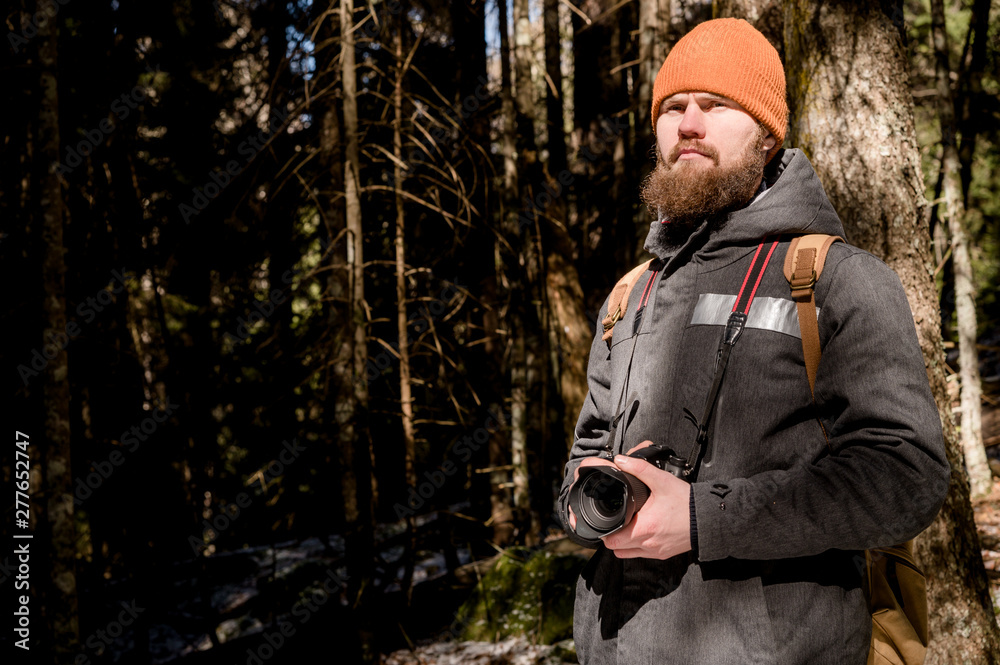 Portrait of a bearded photographer with a reflex camera in his hands in the winter coniferous forest. Photo travel concept