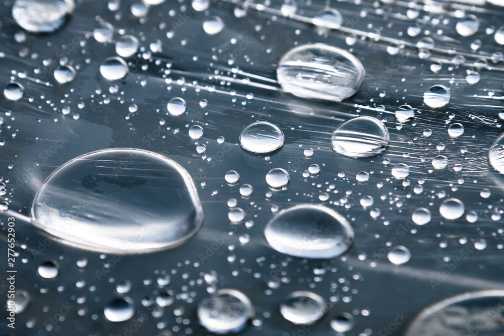 Close-up of raindrops of different sizes on the surface covered with cling film. Moisture weather and humidity concept - obrazy, fototapety, plakaty 