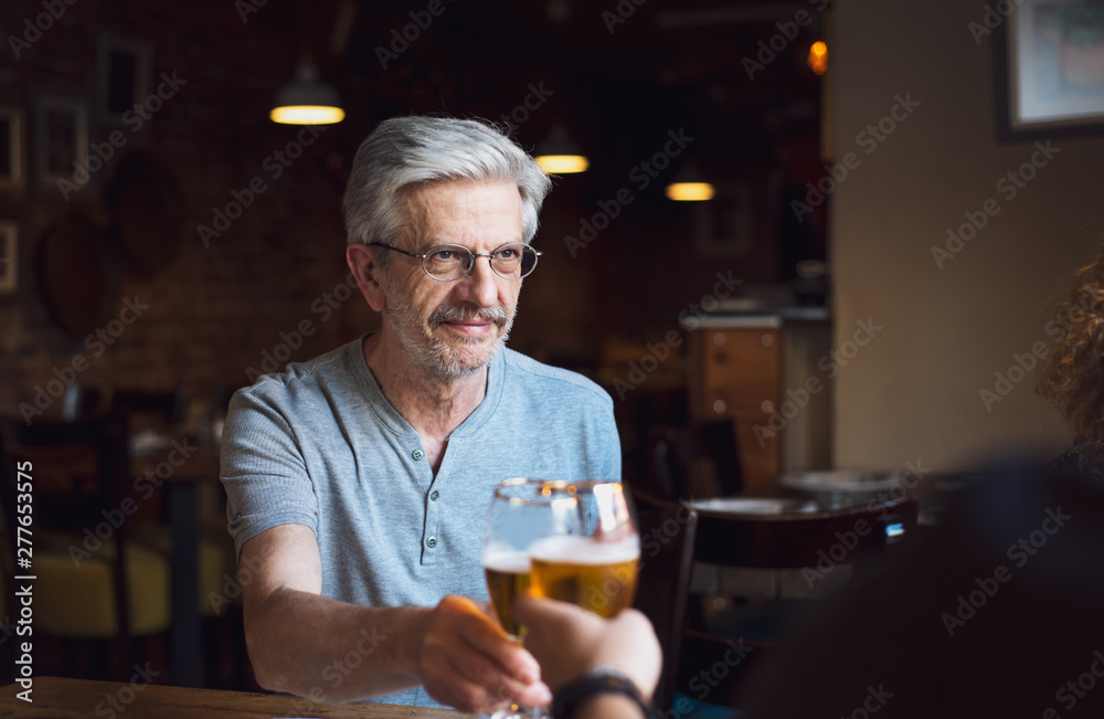 Senior man toasting with a beer in a bar