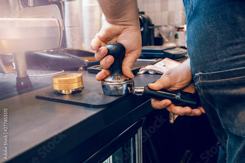 Closeup of barista hands using tamper to press ground coffee into portafilter to make espresso hot drink. Small local business work in cafe.