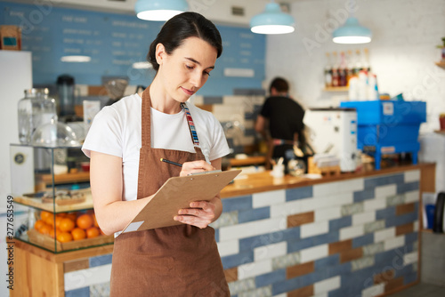 Barista standing while writing in the notepad.