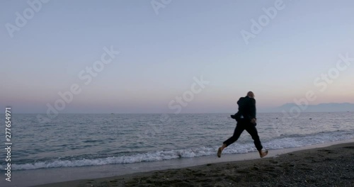 Happy adult bald man with glasses and business suit, quietly walking barefoot along the calm evening sea. photo
