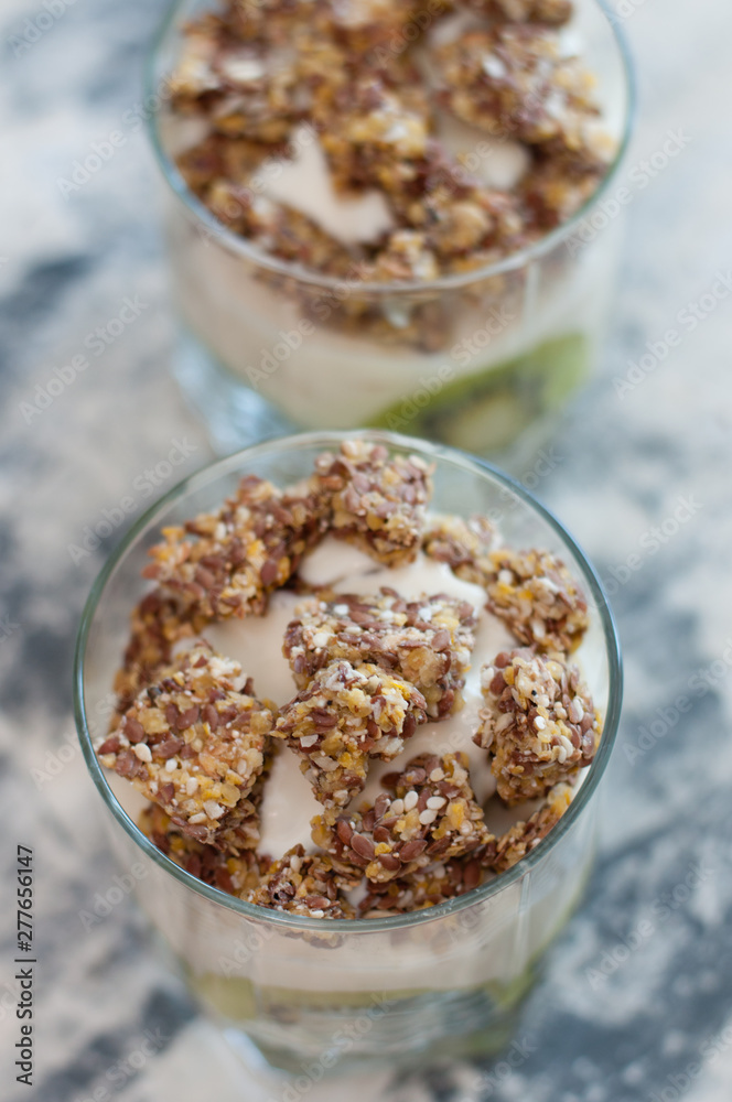 Granola, kiwi, banana and Greek yogurt in two glass cups on gray concrete, close-up view from the top Granola, kiwi, banana and Greek yogurt in two glass cups on gray concrete, close-up view from the top