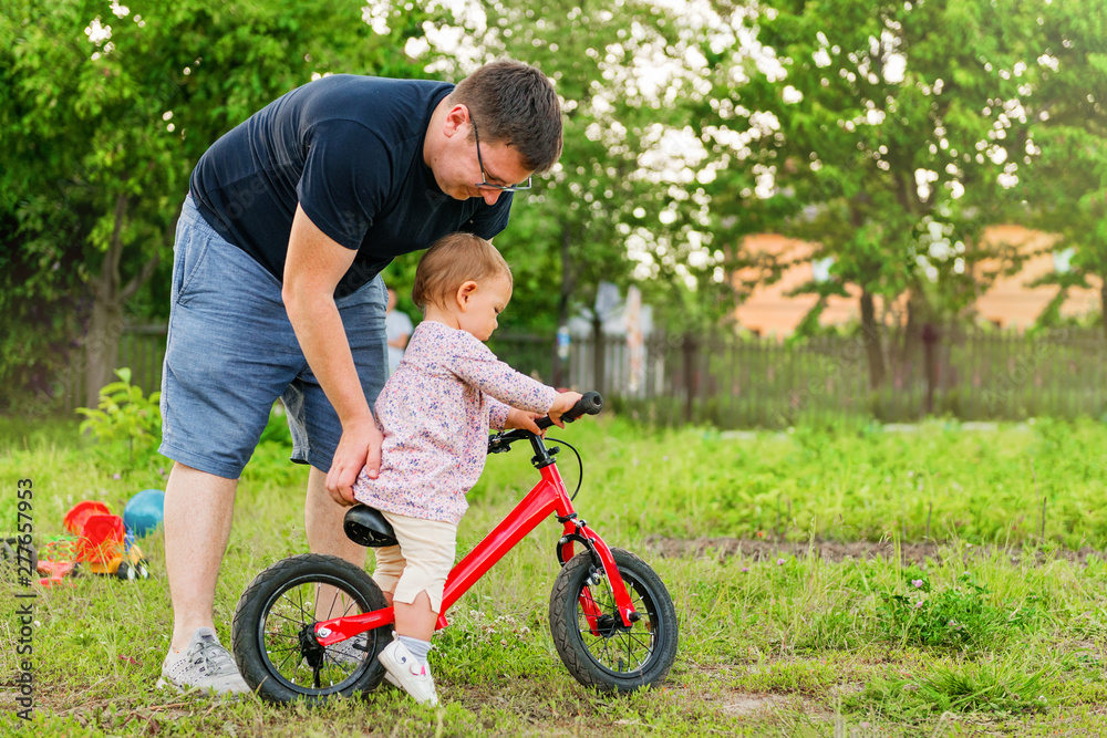 Fototapeta premium Young father spend time with Cute little one years old toddler girl child and balance bike, father's day