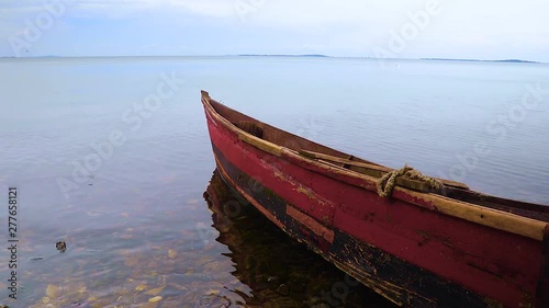 Small red wooden fishing boat lies in shallow water by coast of Lake Victoria. Outline of island visible by distant horizon. photo