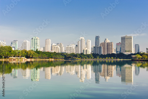Buildings and trees reflex in a lake of public park © NUTTANART